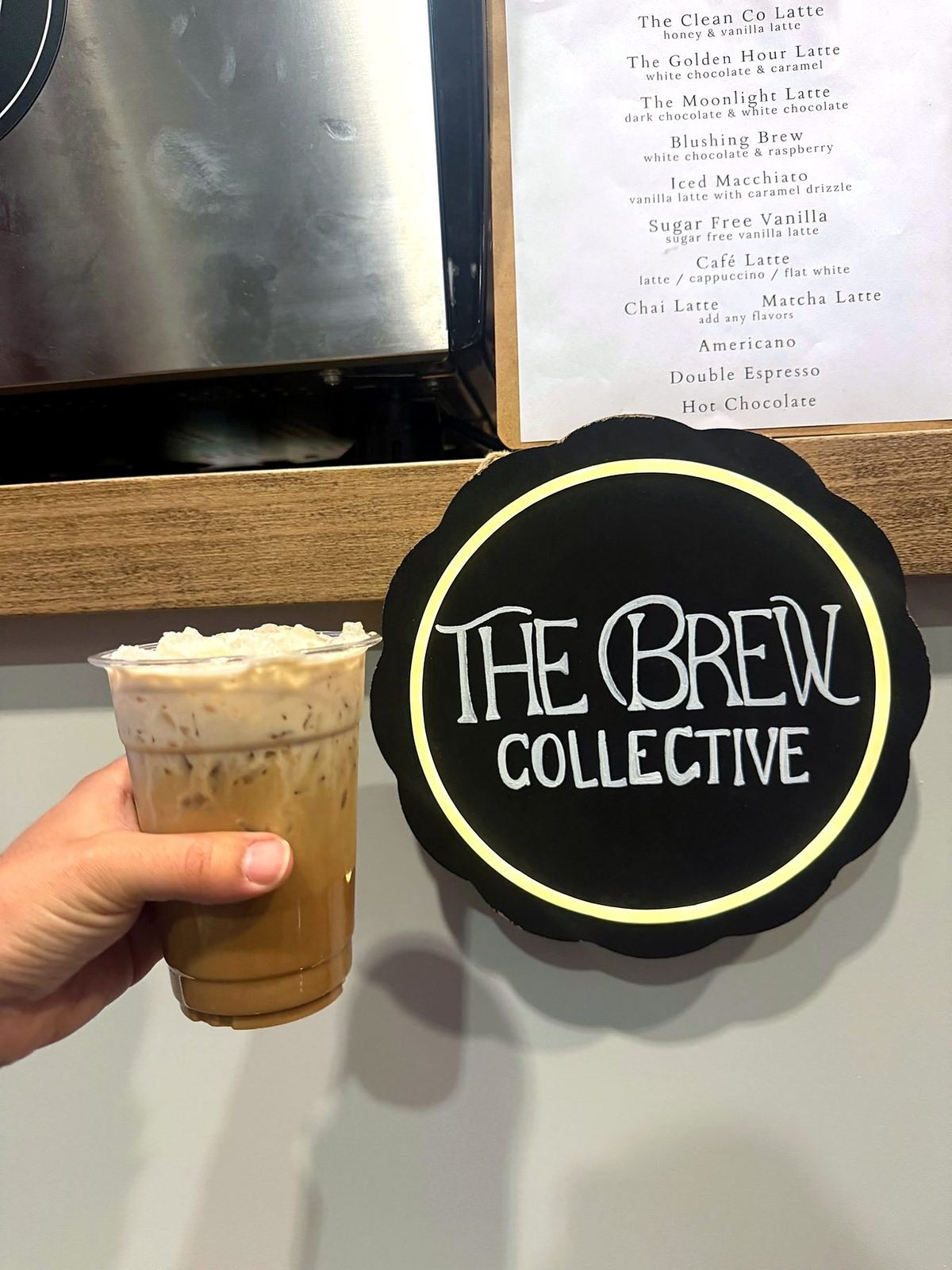 Iced latte in front of The Brew Collective sign and café menu