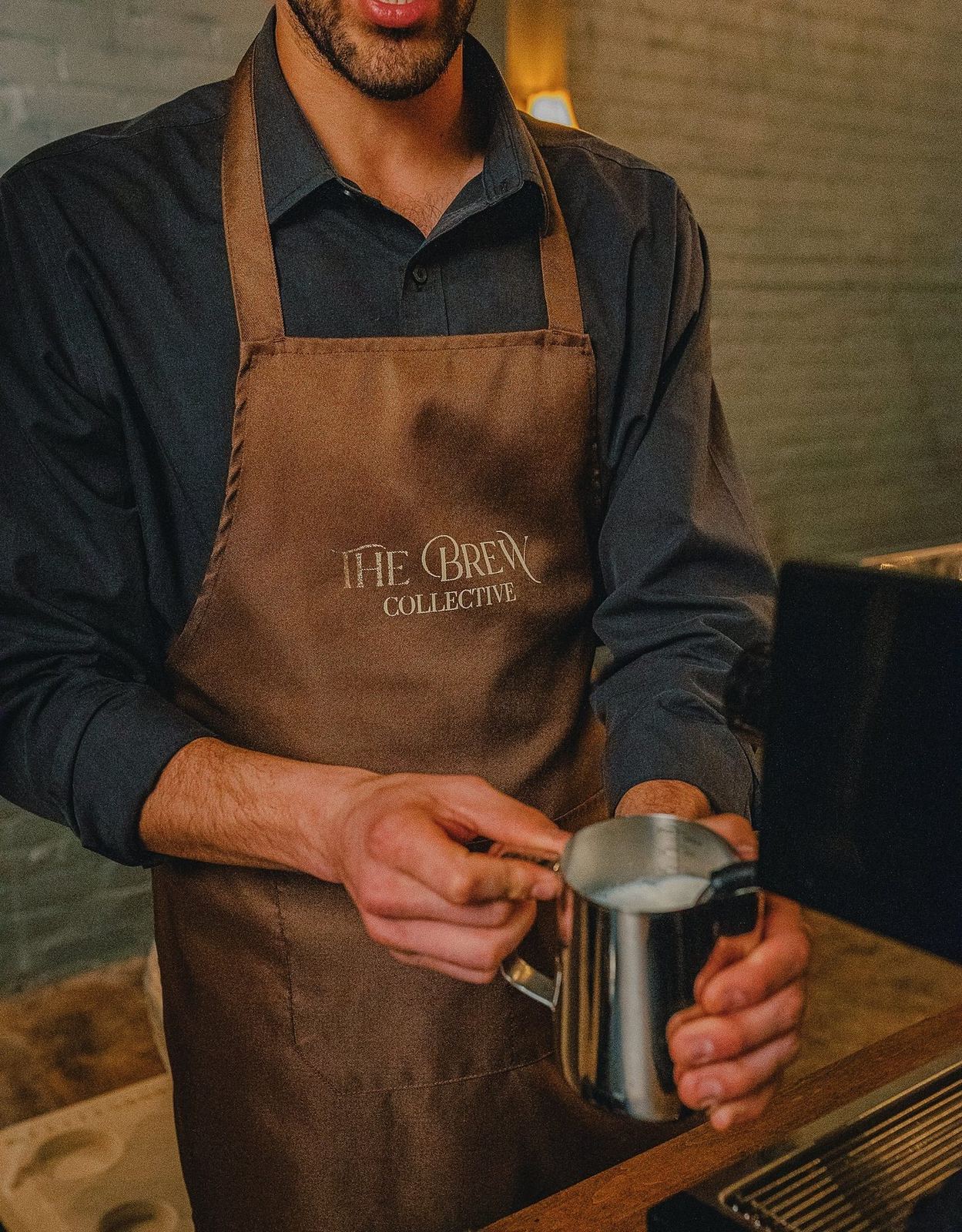 Barista in a Brew Collective apron steaming milk